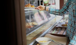 Corporate employee selecting a hot meal from office cafeteria serving line.